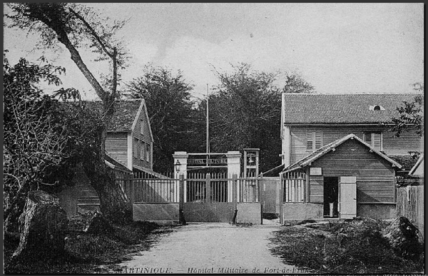 Tanlistwa, carte postale en noir et blanc montrant le portail de l'ancien Hôpital militaire de Fort-de-France avec un petit cabanon de gardien sur la droite